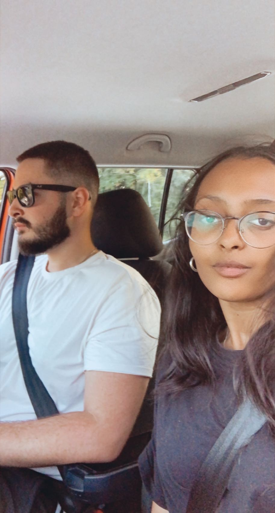 Two friends wearing seat belts inside a car, captured in a selfie