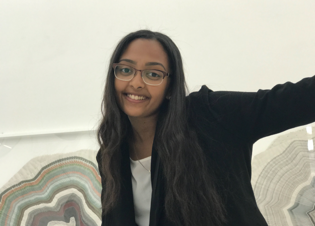 A smiling woman in glasses sitting indoors beside patterned cushions