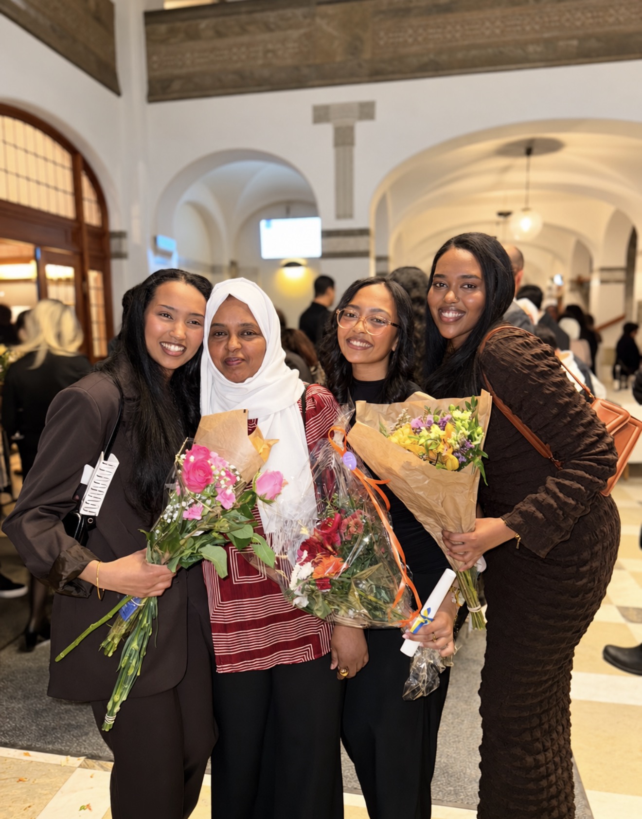 Four women smiling together indoors with colourful bouquets of flowers
