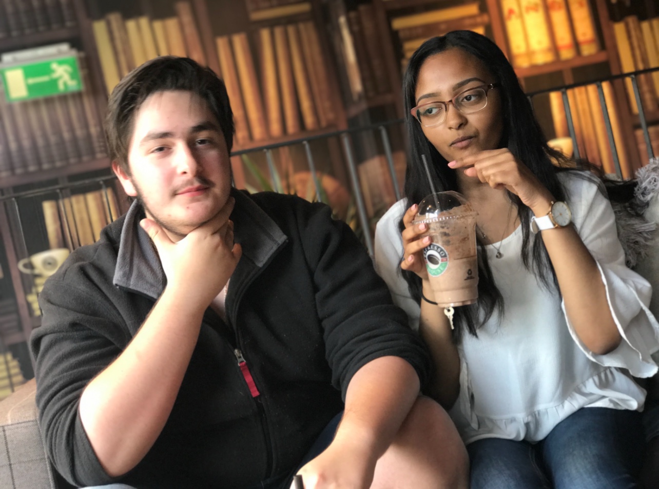 Two friends sitting together in a cafe, one holding an iced drink